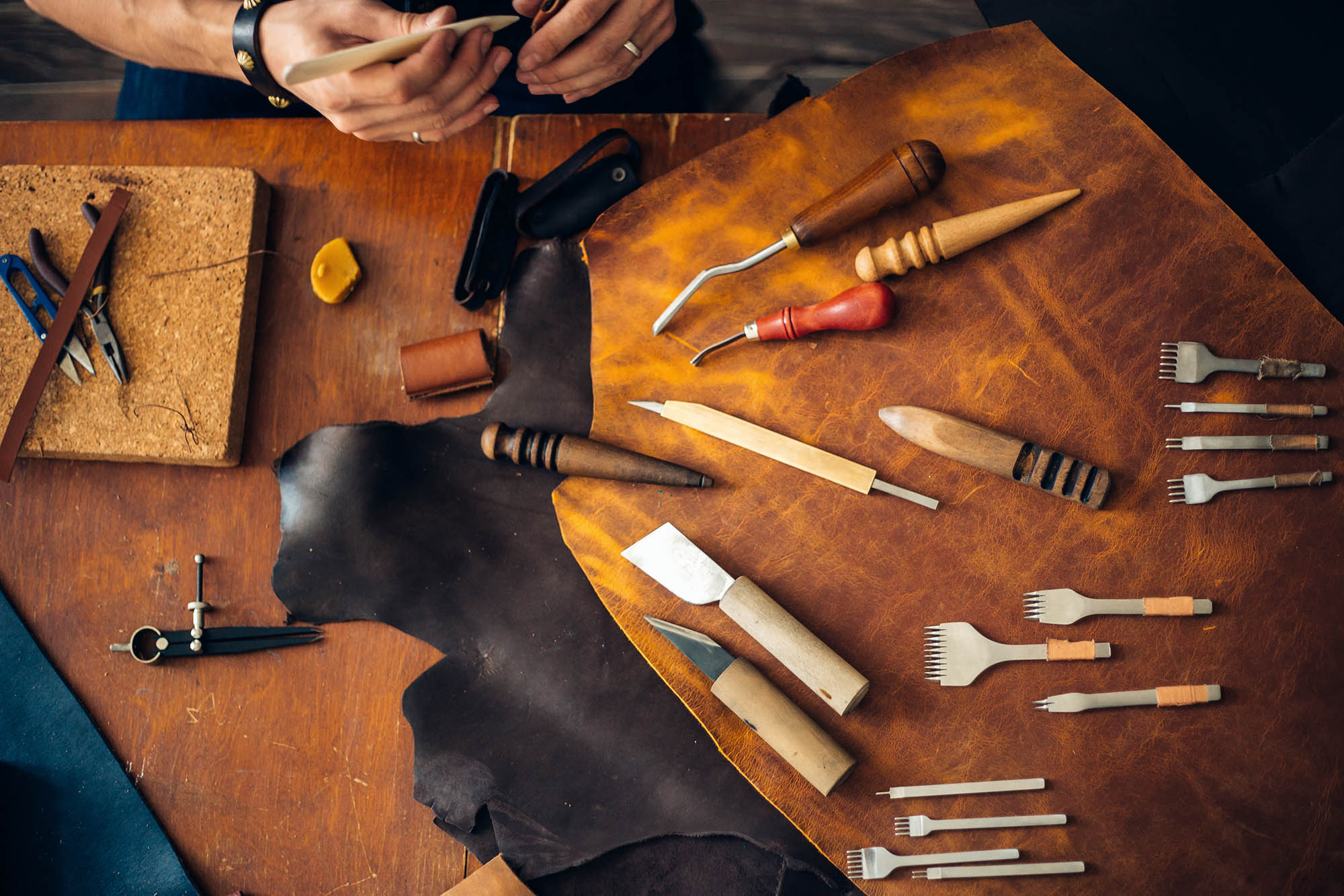 man doing leatherwork with leatherworking tools on table